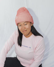 Person wearing a pink beanie and sweater against a white background