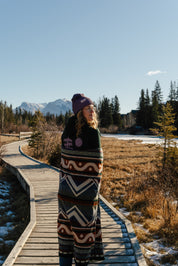Blanket, shades of blue, orange, lightweight, mountain designs, handcrafted in Ecuador, Acrylic, durable, 70" x 48", soft, camping, van life, outdoors, lifestyle, Les Saisons, Marine Poiraton ski Blanket Mountains orange and green.