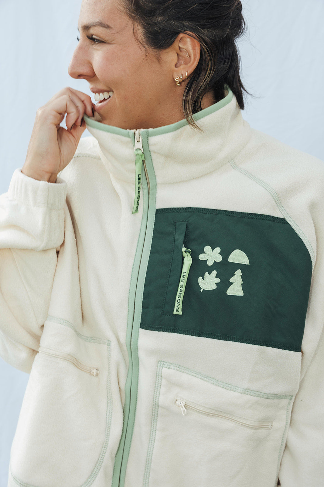 Person wearing a cream and green jacket with a logo on a light gray background détails women