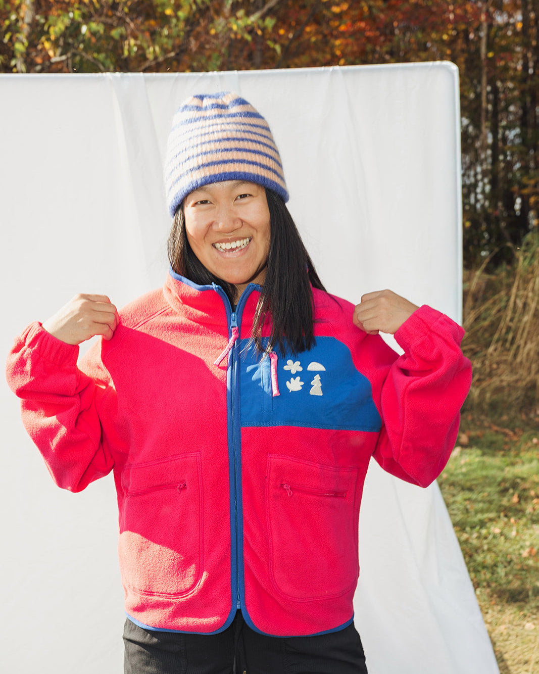 Person wearing a red and blue fleece jacket les Saisons with a colorful knit hat in an outdoor setting.