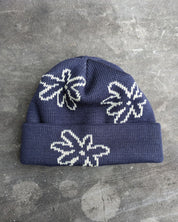 Navy beanie with white flowers with a les Saisons tag on a gray concrete surface, made in Canada.