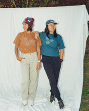 Two people standing in front of a white backdrop with trees in the background with flower Power Tshirts from les Saisons