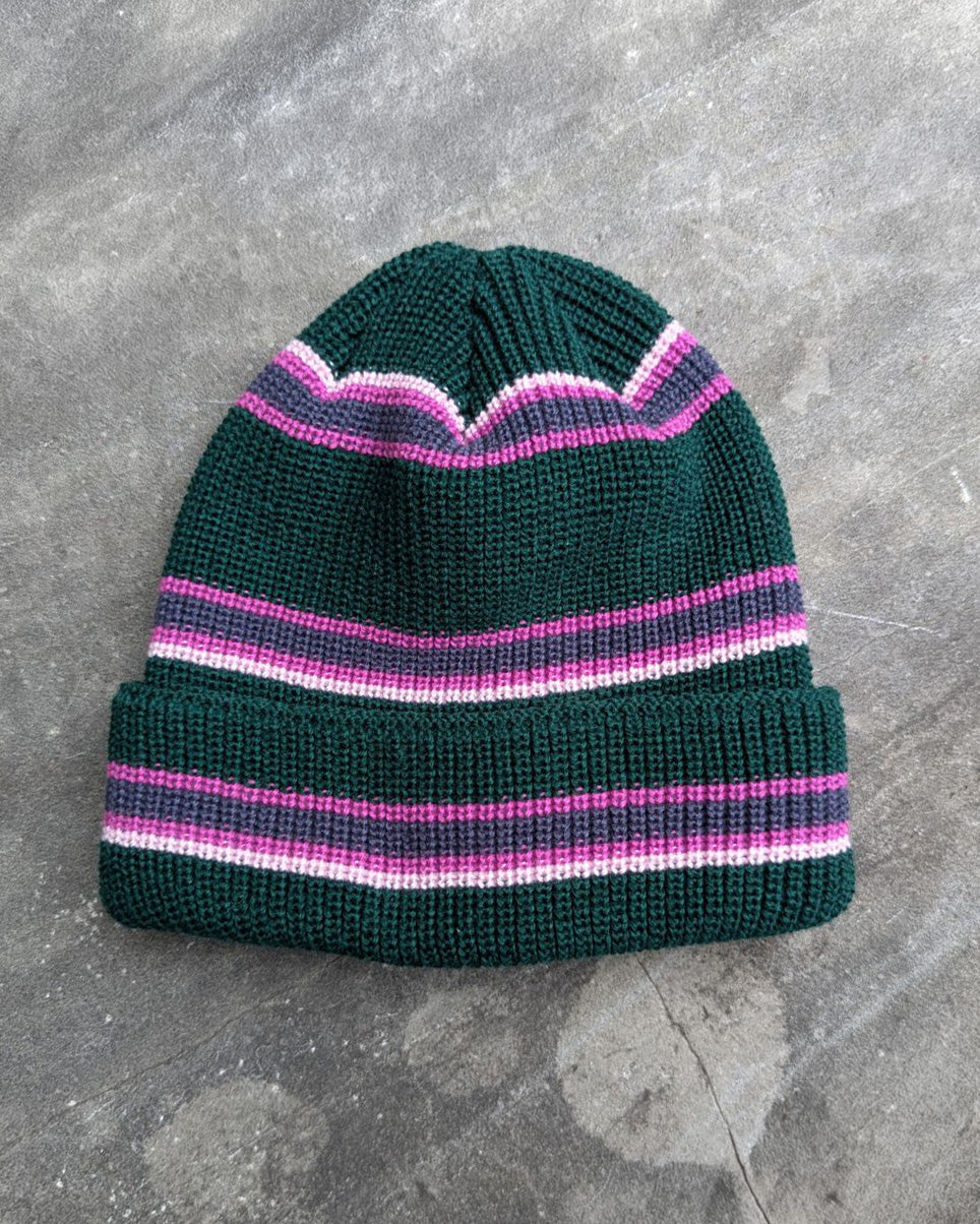 Green and pink retro striped beanie with a les Saisons tag on a gray concrete surface, made in Canada.