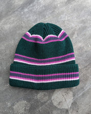 Green and pink retro striped beanie with a les Saisons tag on a gray concrete surface, made in Canada.