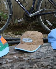 brown cap featuring a logo on a wooden surface with a bicycle in the background