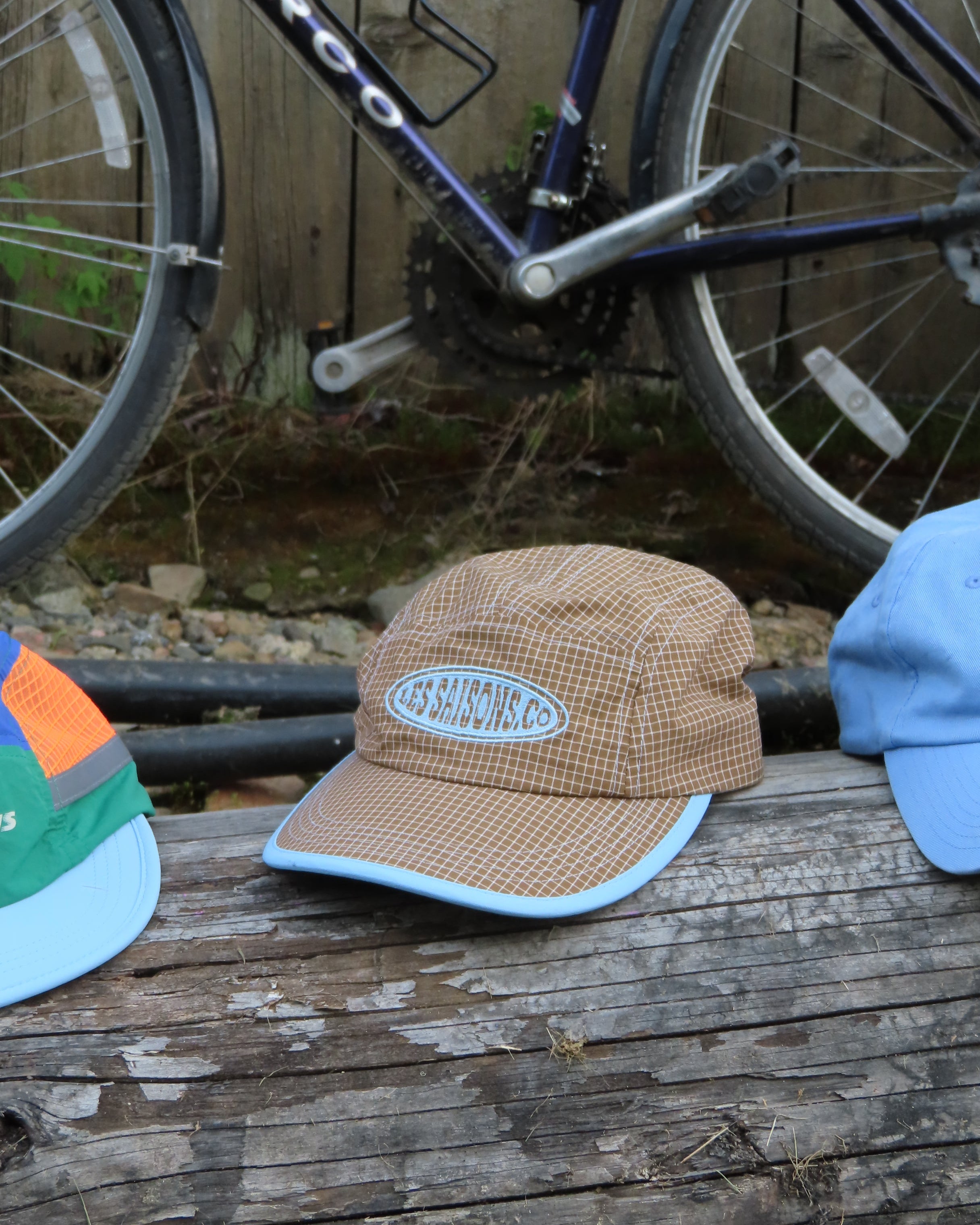 brown cap featuring a logo on a wooden surface with a bicycle in the background