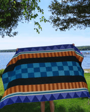 Person holding a colorful striped blanket on a pole with trees and grass in the background