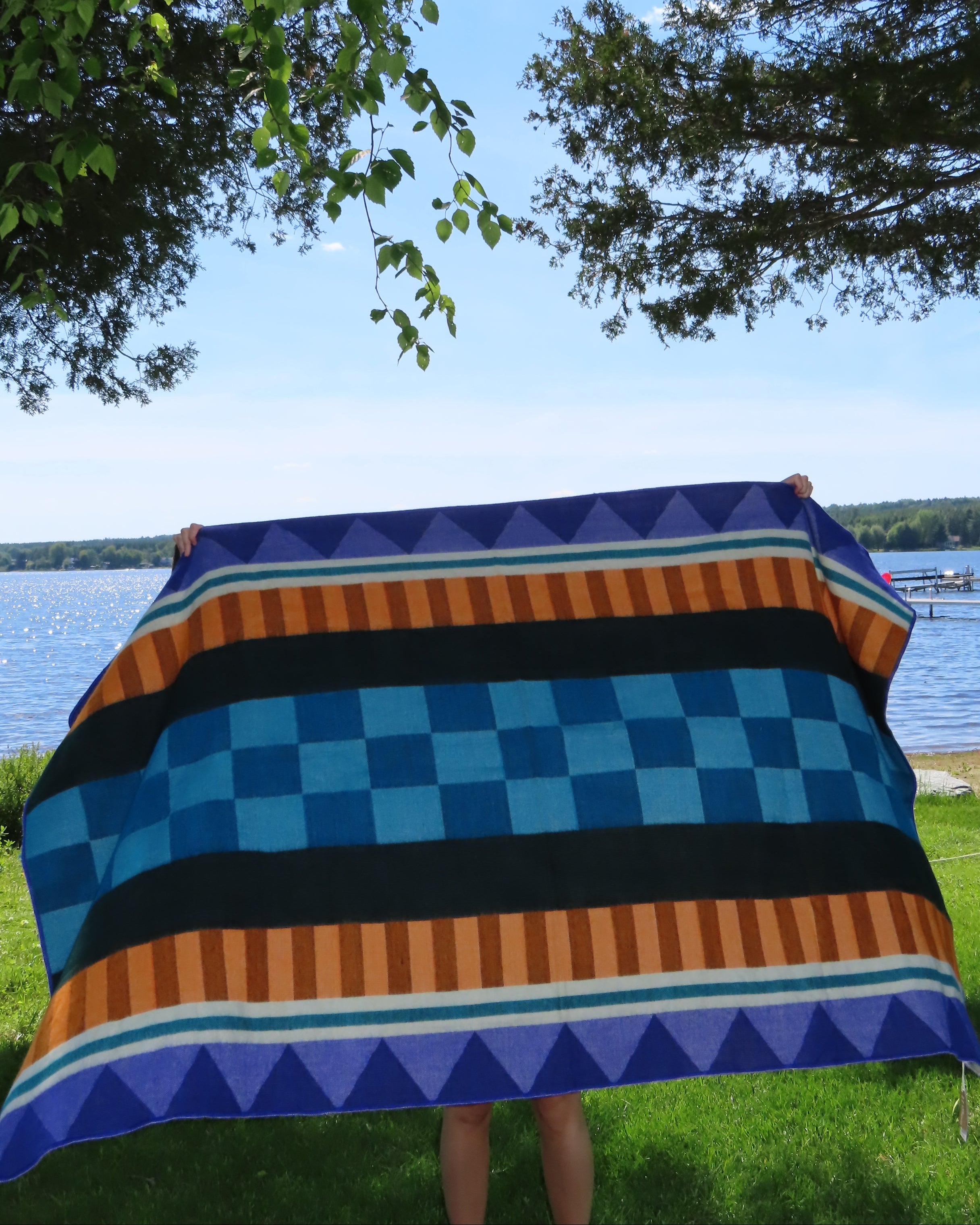 Person holding a colorful striped blanket on a pole with trees and grass in the background