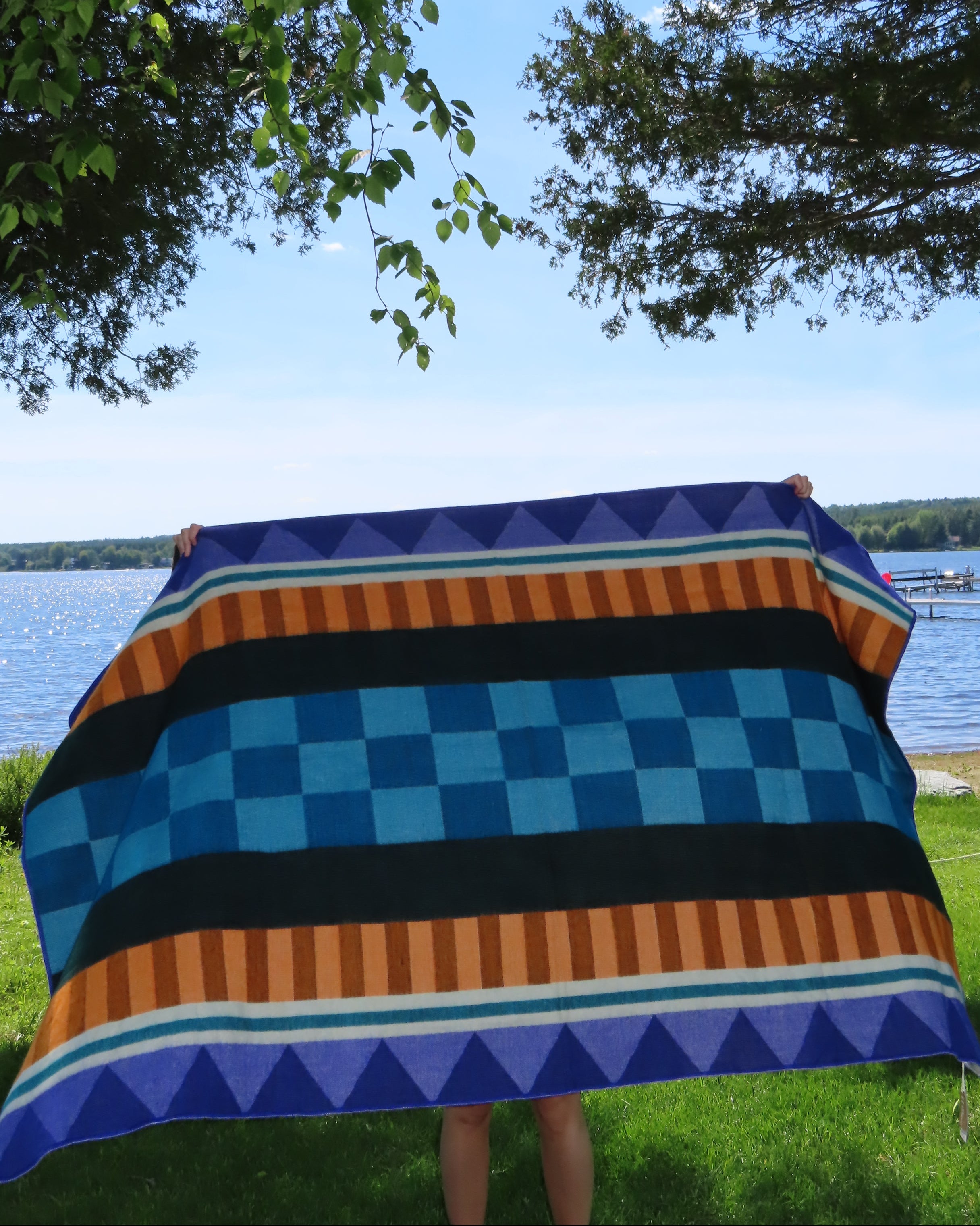 Person holding a colorful striped blanket on a pole with trees and grass in the background