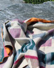 Colorful patterned pink blanket over a stone surface with grass in the background