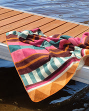 Colorful striped pink blanket hanging on a dock with water in the background