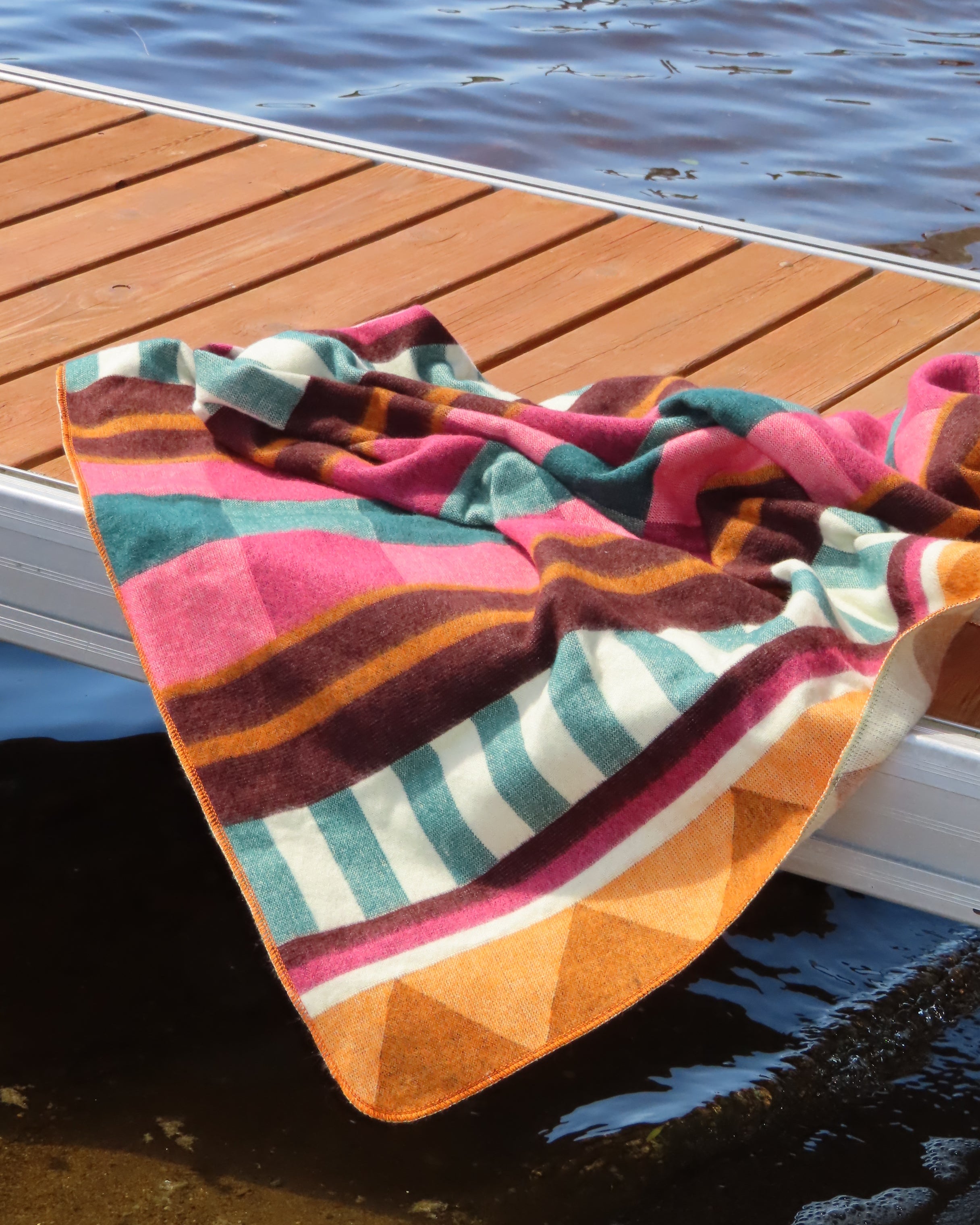 Colorful striped pink blanket hanging on a dock with water in the background