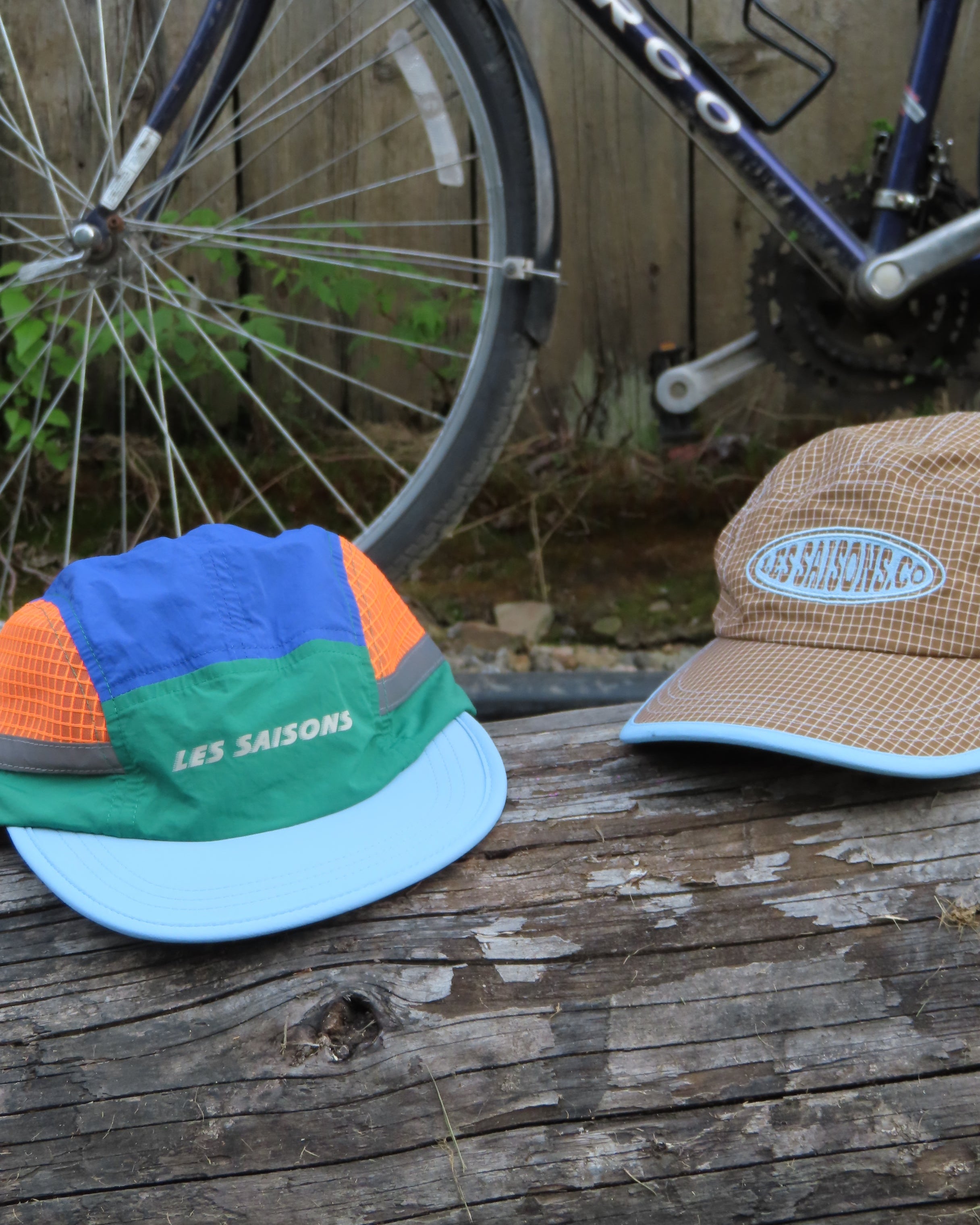 Colorful cap and brown hat on a wooden surface with a bicycle wheel in the foreground.