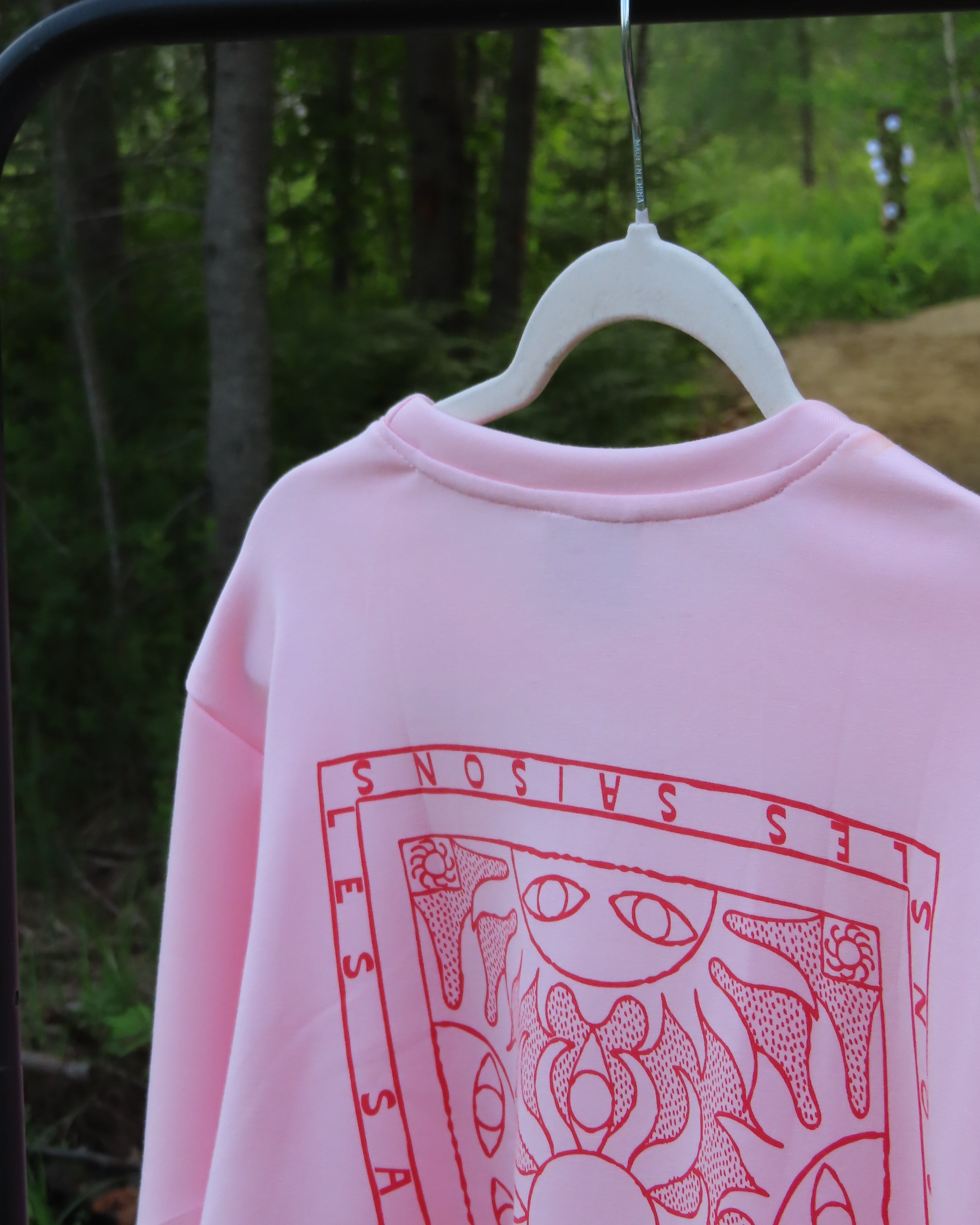Pink shirt with red graphic design on a hanger against a green background
