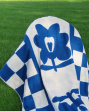 Blue and white checkered blanket with a flower logo on a green grass background