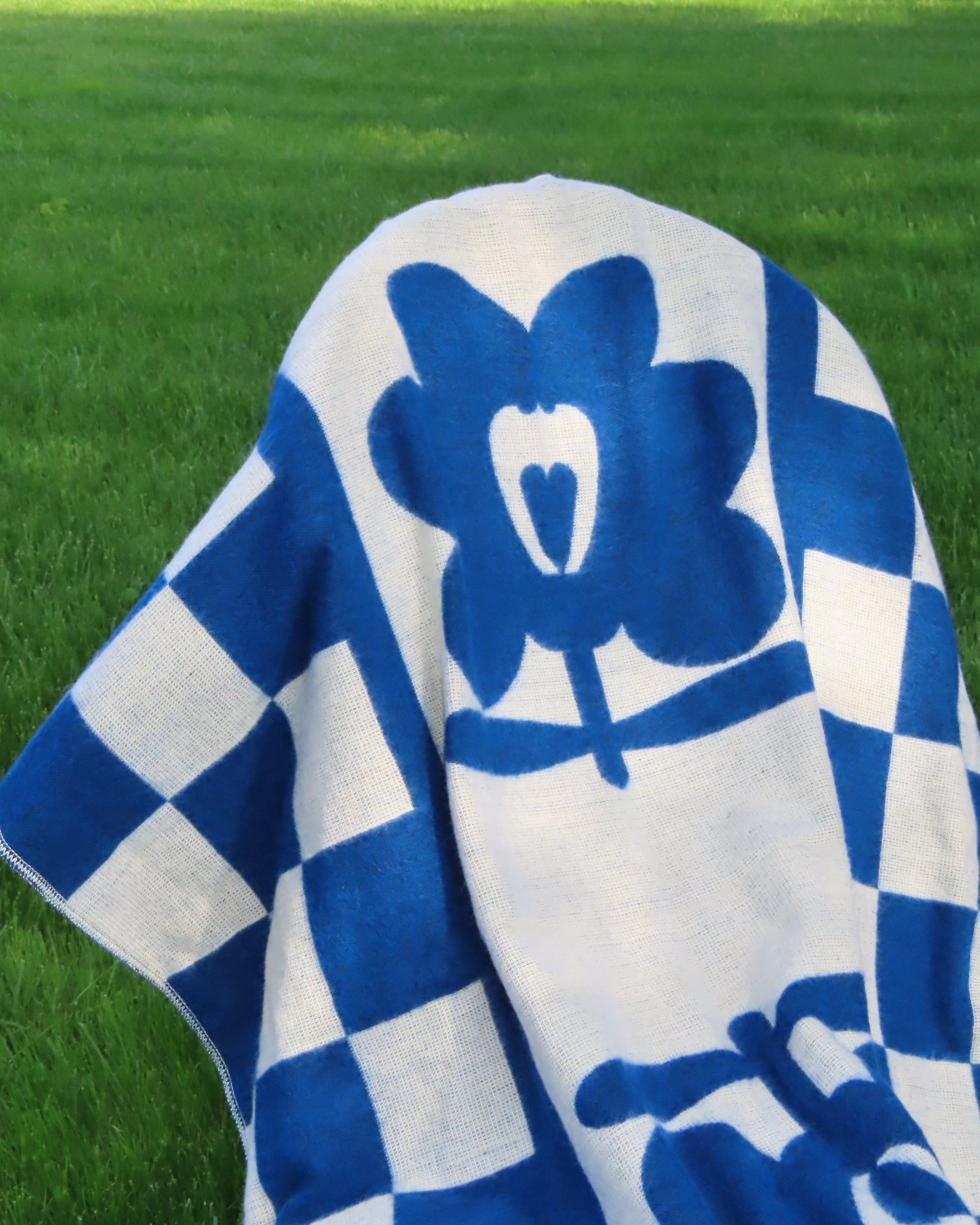 Blue and white checkered blanket with a flower logo on a green grass background