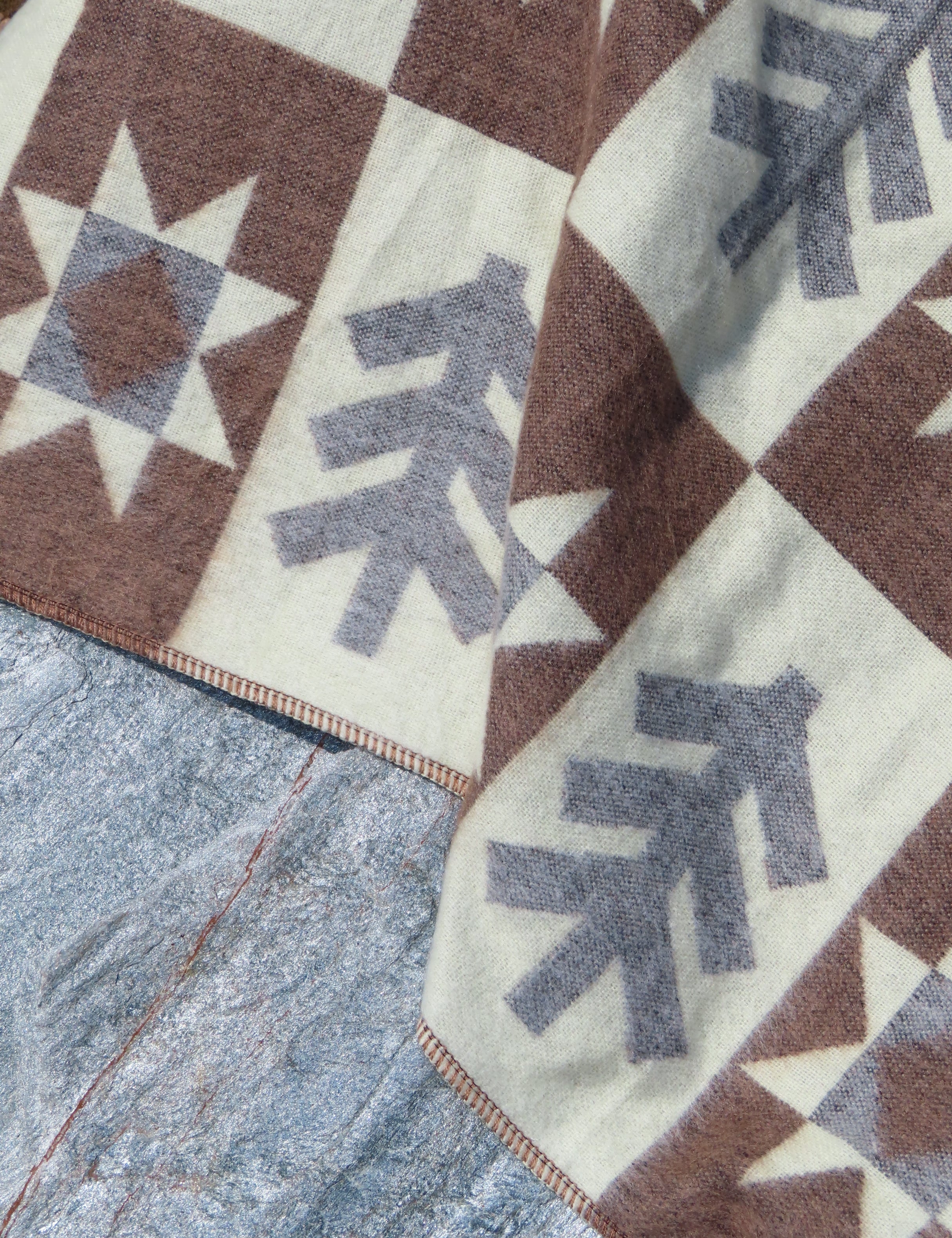 Close up of a brown blanket wiht a forest pattern laying on a rock