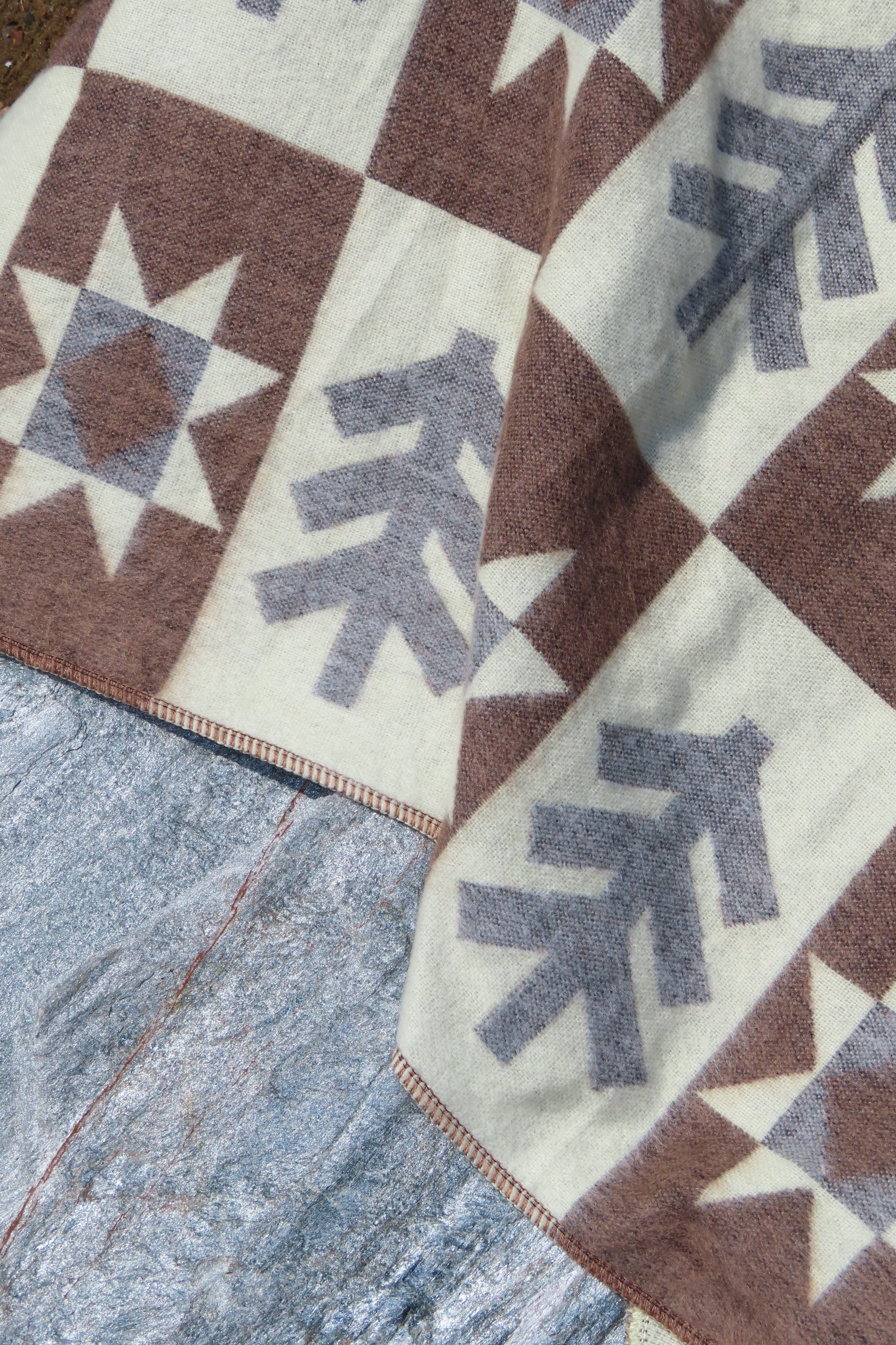 Close up of a brown blanket wiht a forest pattern laying on a rock