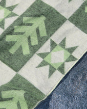 Close up of a green and beige blanket with a foresy pattern
