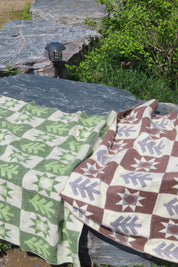A green blanket with a brown blanket with forest pattern laying on a rock