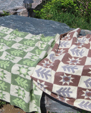 A green blanket with a brown blanket with a forest pattern laying on a rock