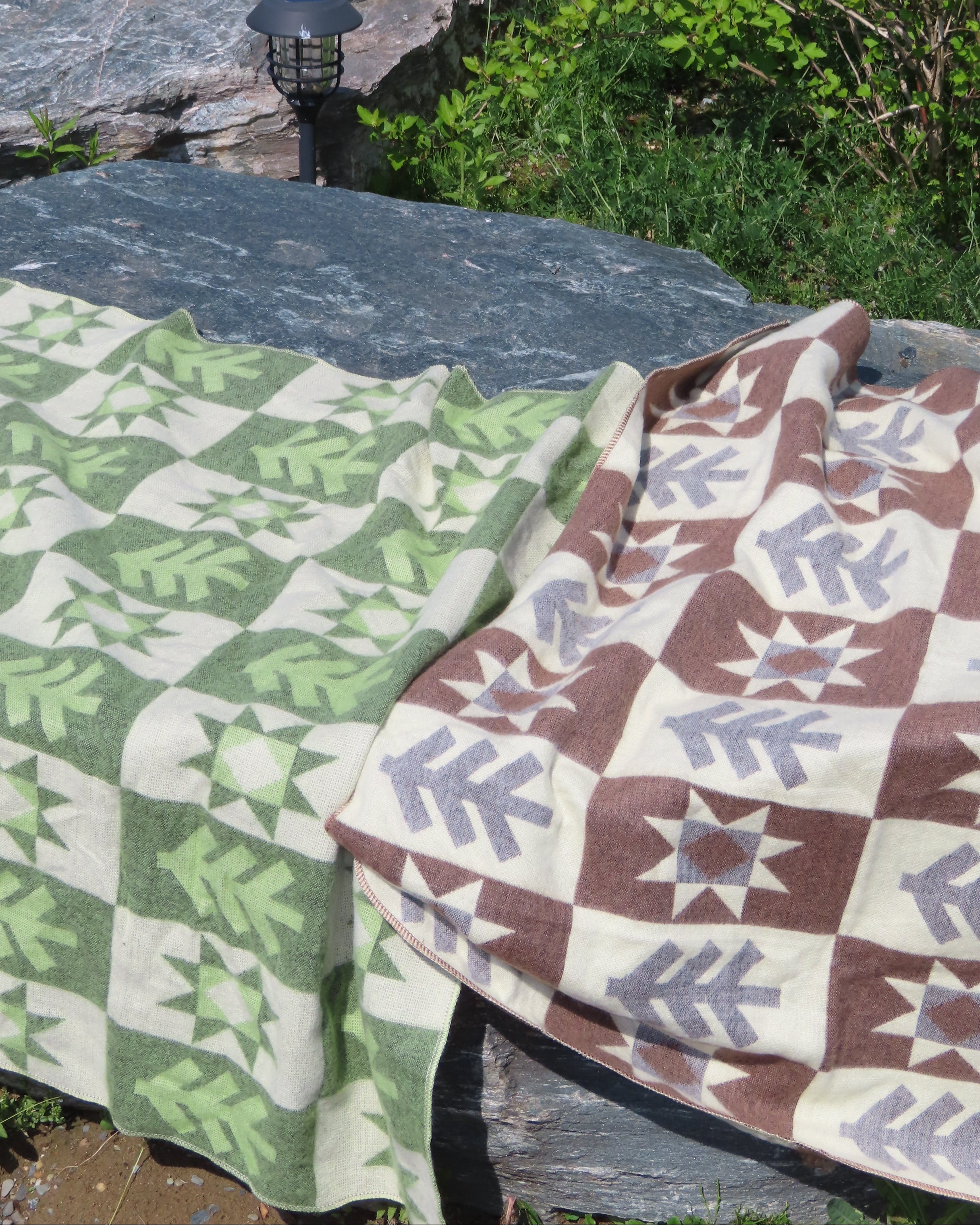 A green blanket with a brown blanket with a forest pattern laying on a rock