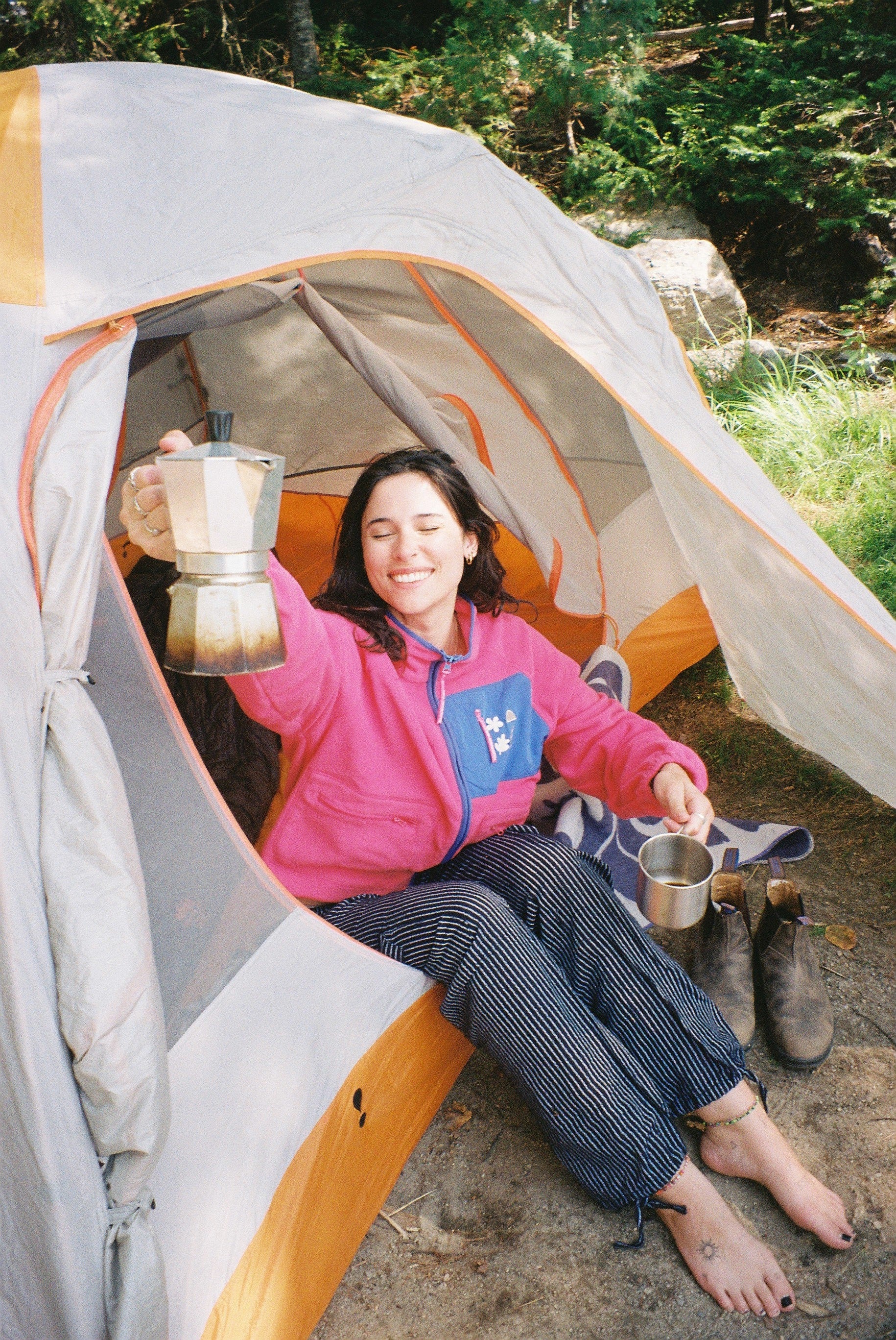 Outdoorsy women inside a tent holding a coffee pot with a scenic background with an fleece jacket from the brand les Saisons