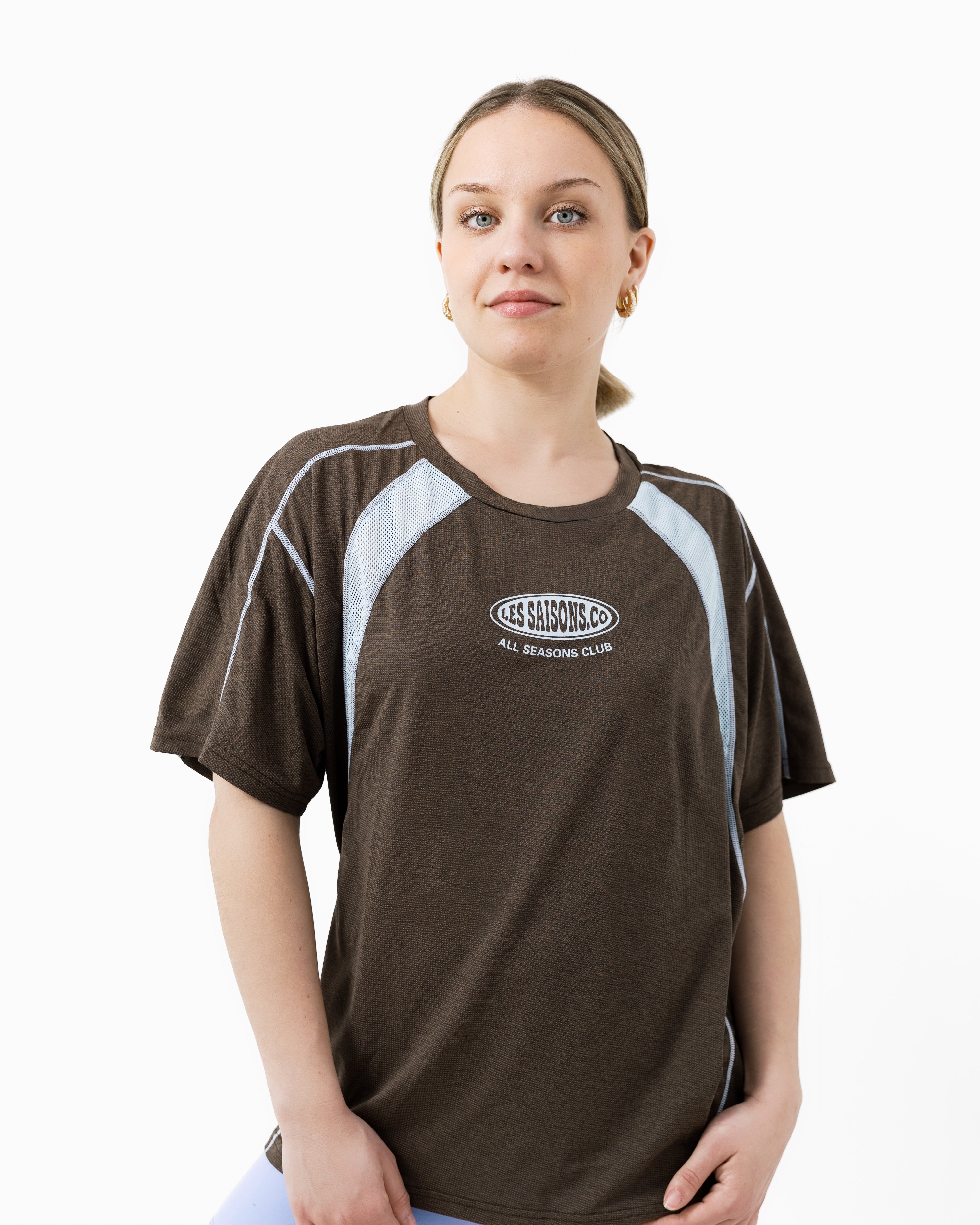 Woman wearing a brown sports t-shirt with Les Saisons logo on a white background