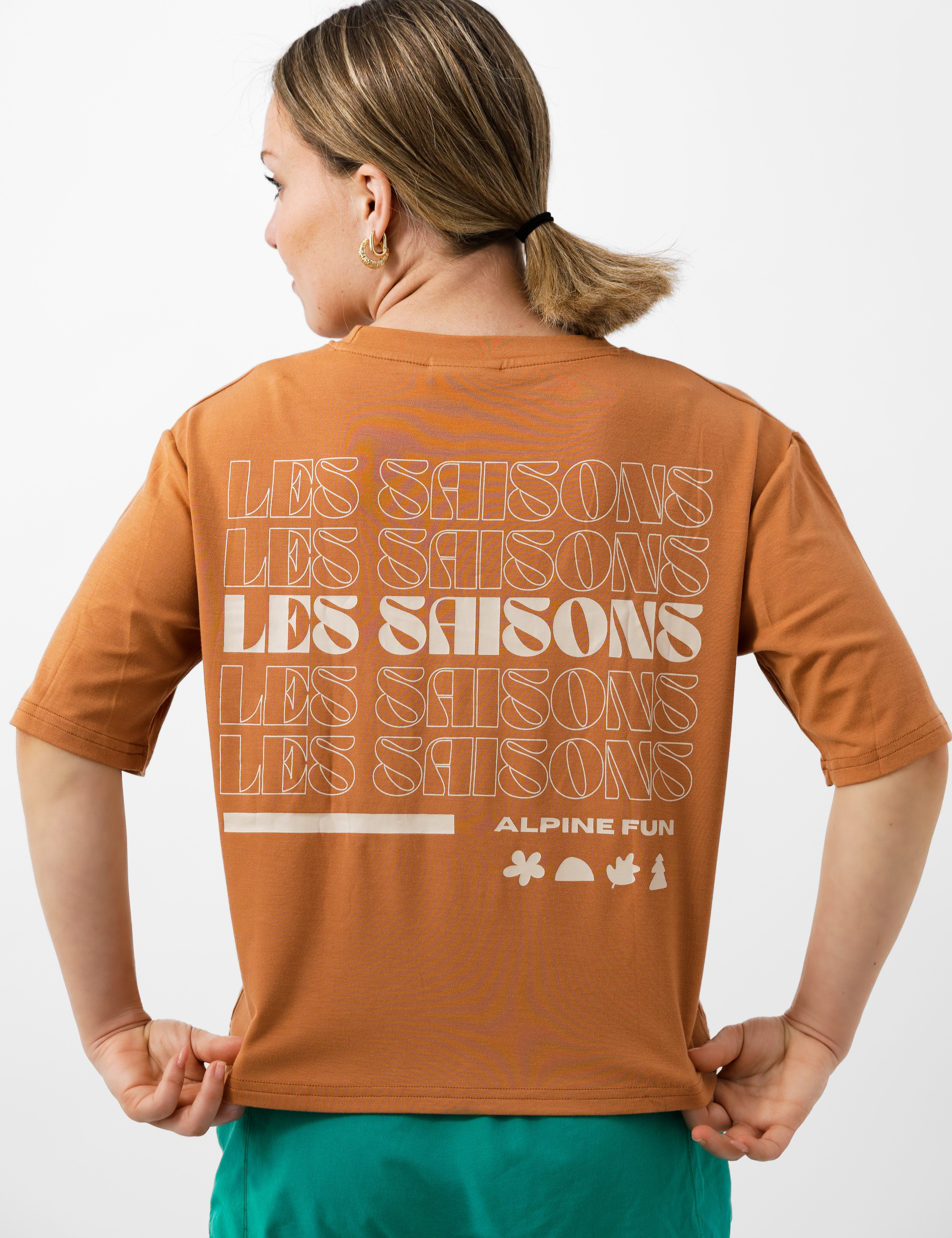 Person wearing an brown t-shirt with Les Saisons on the back, standing against a white background