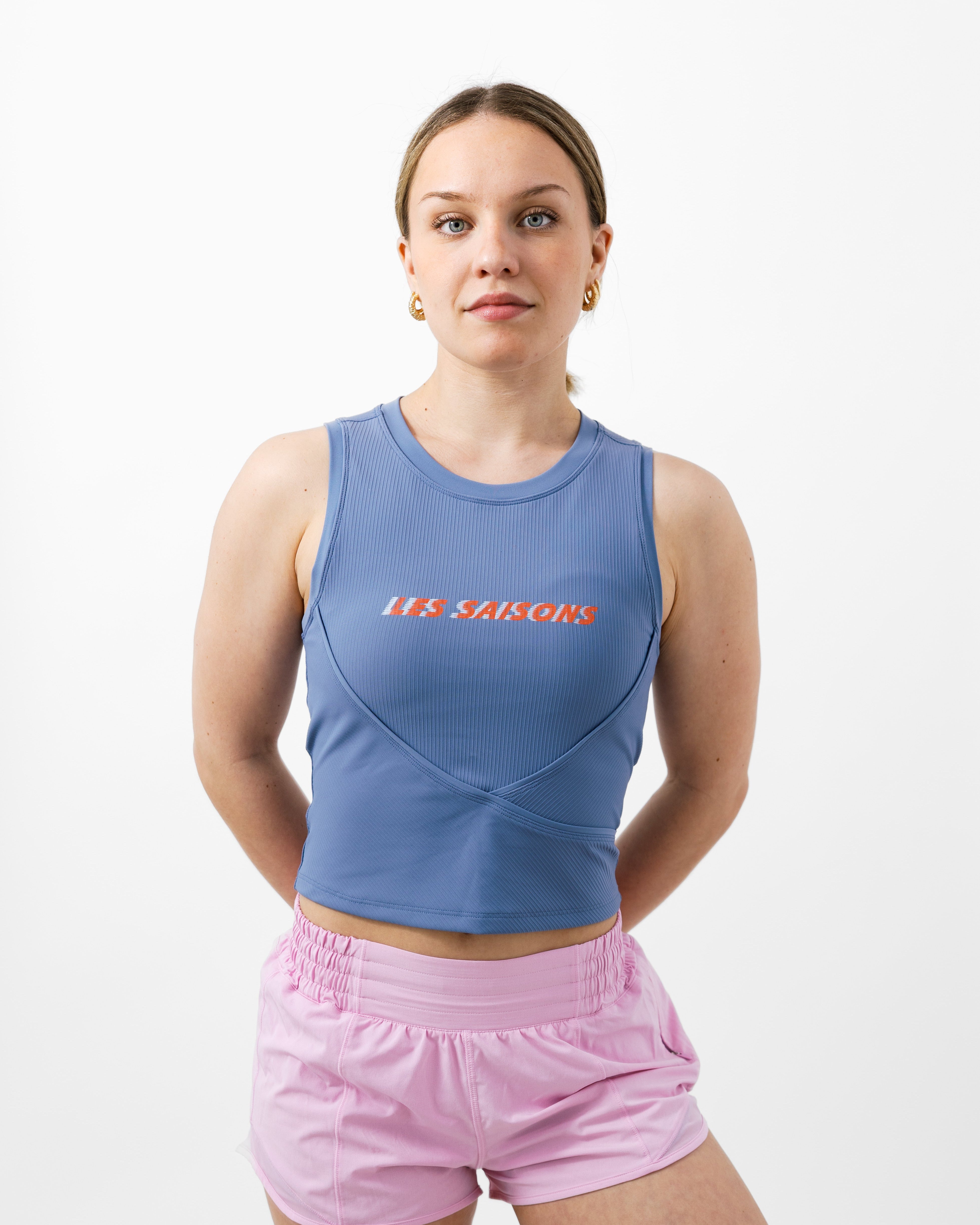 Woman wearing a purple ribbed tank top with pink shorts and white background