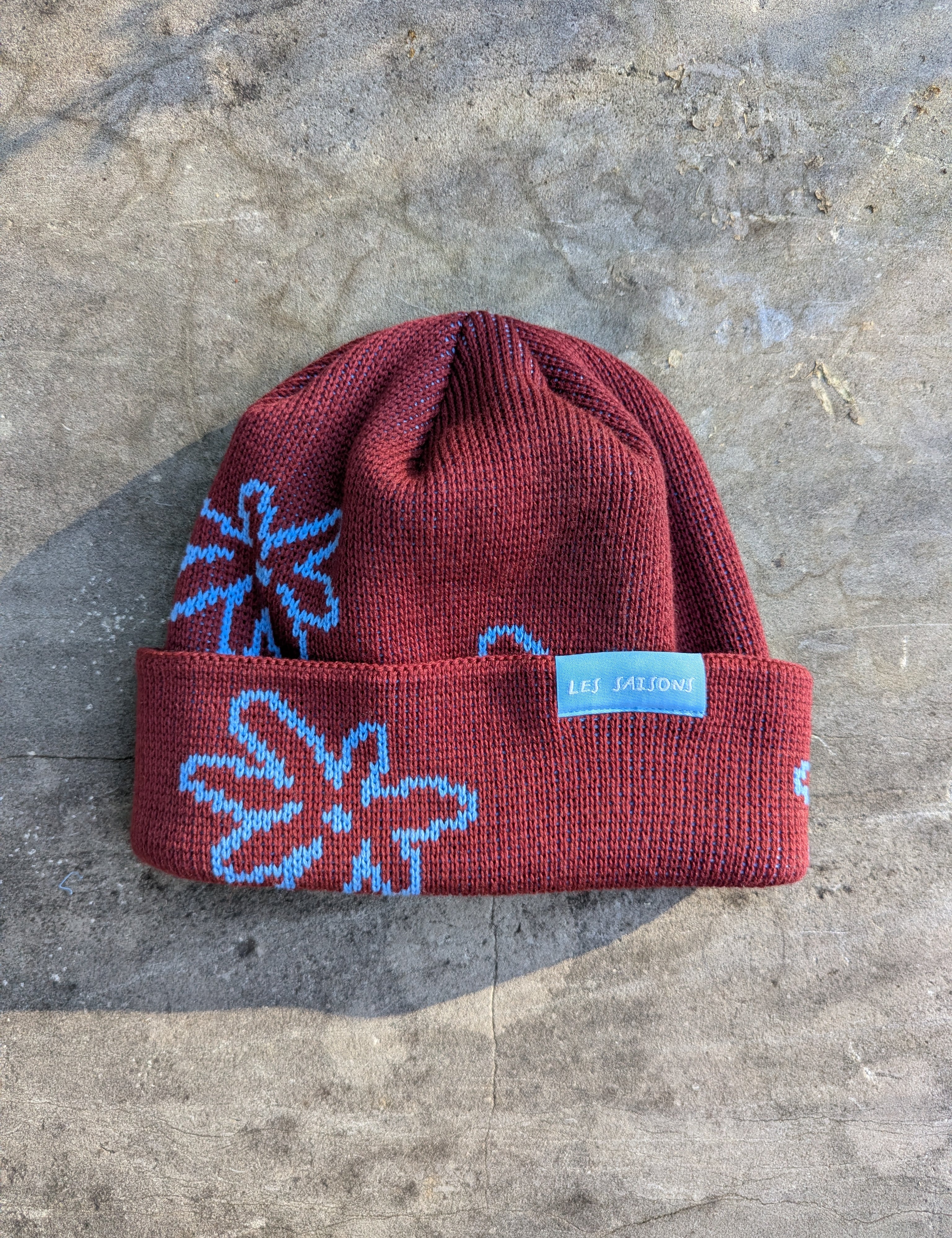 Red beanie with blue floral patterns on a gray surface Les Saisons.