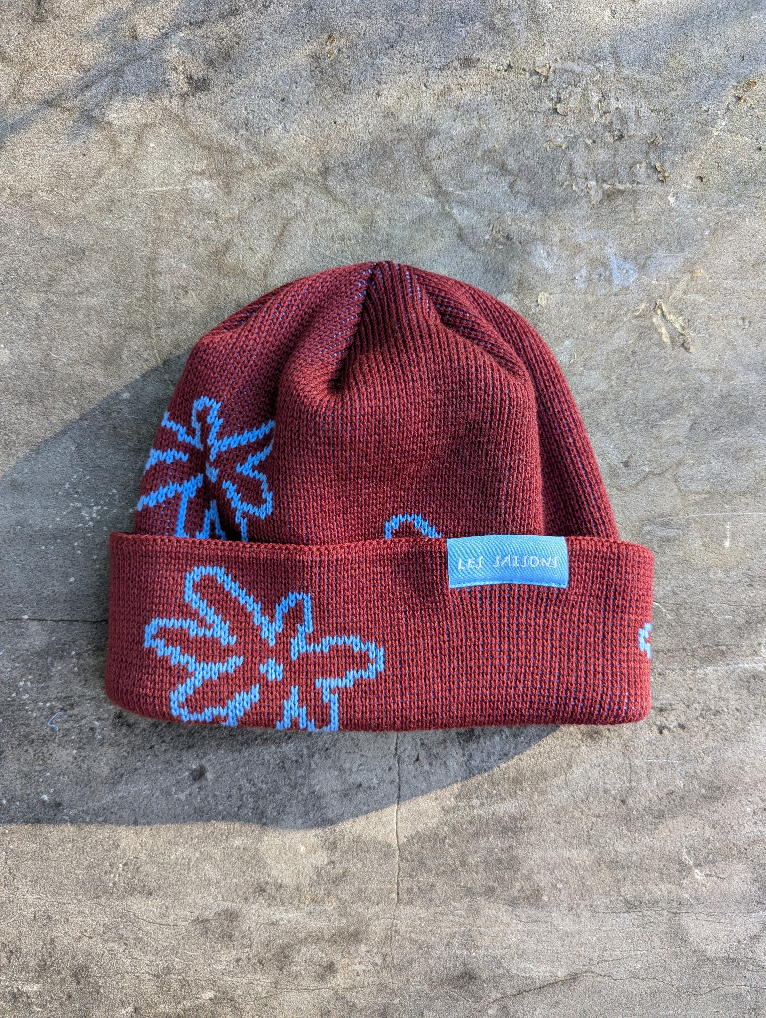 Red beanie with blue floral patterns on a gray surface Les Saisons.