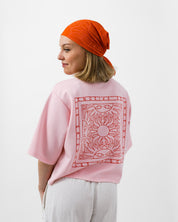 Person wearing a pink shirt with a red pattern and an orange headscarf on a white background