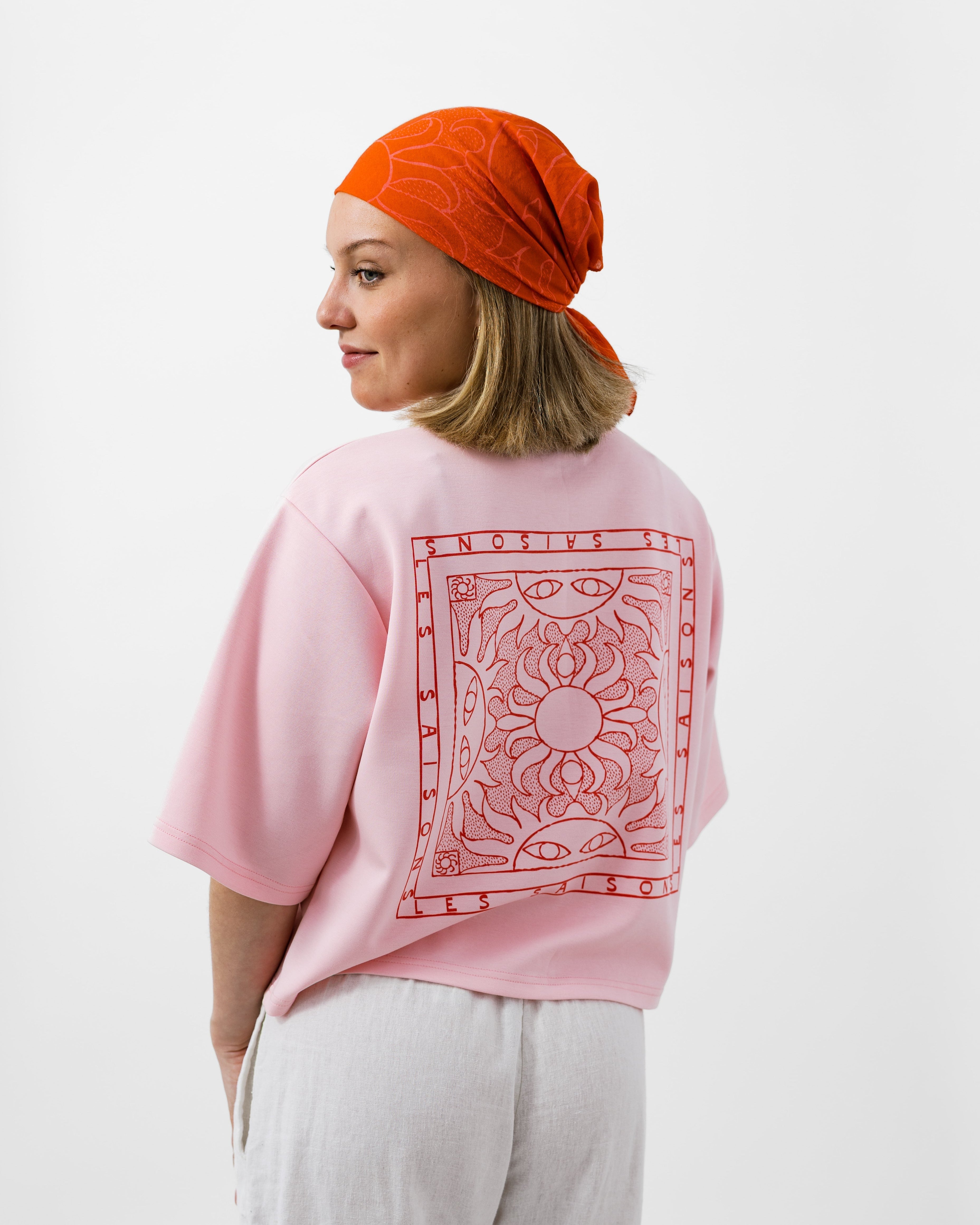 Person wearing a pink shirt with a red pattern and an orange headscarf on a white background