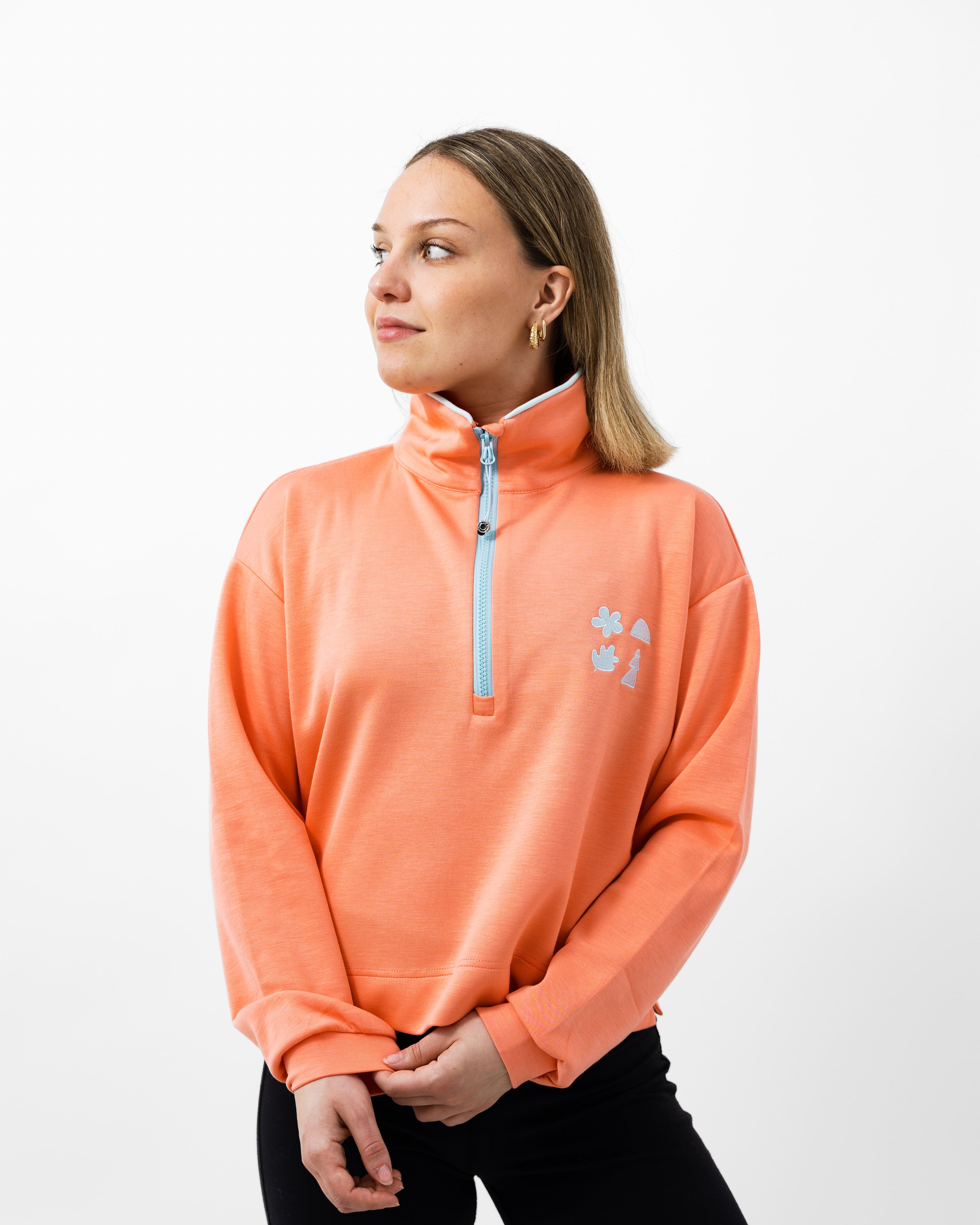 Woman wearing an pink quarter zip with light blue zipper on a white background