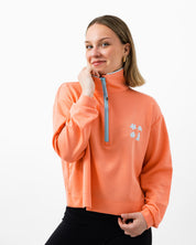 Woman smiling wearing a pink quarter zip with a light blue zipper on a white background