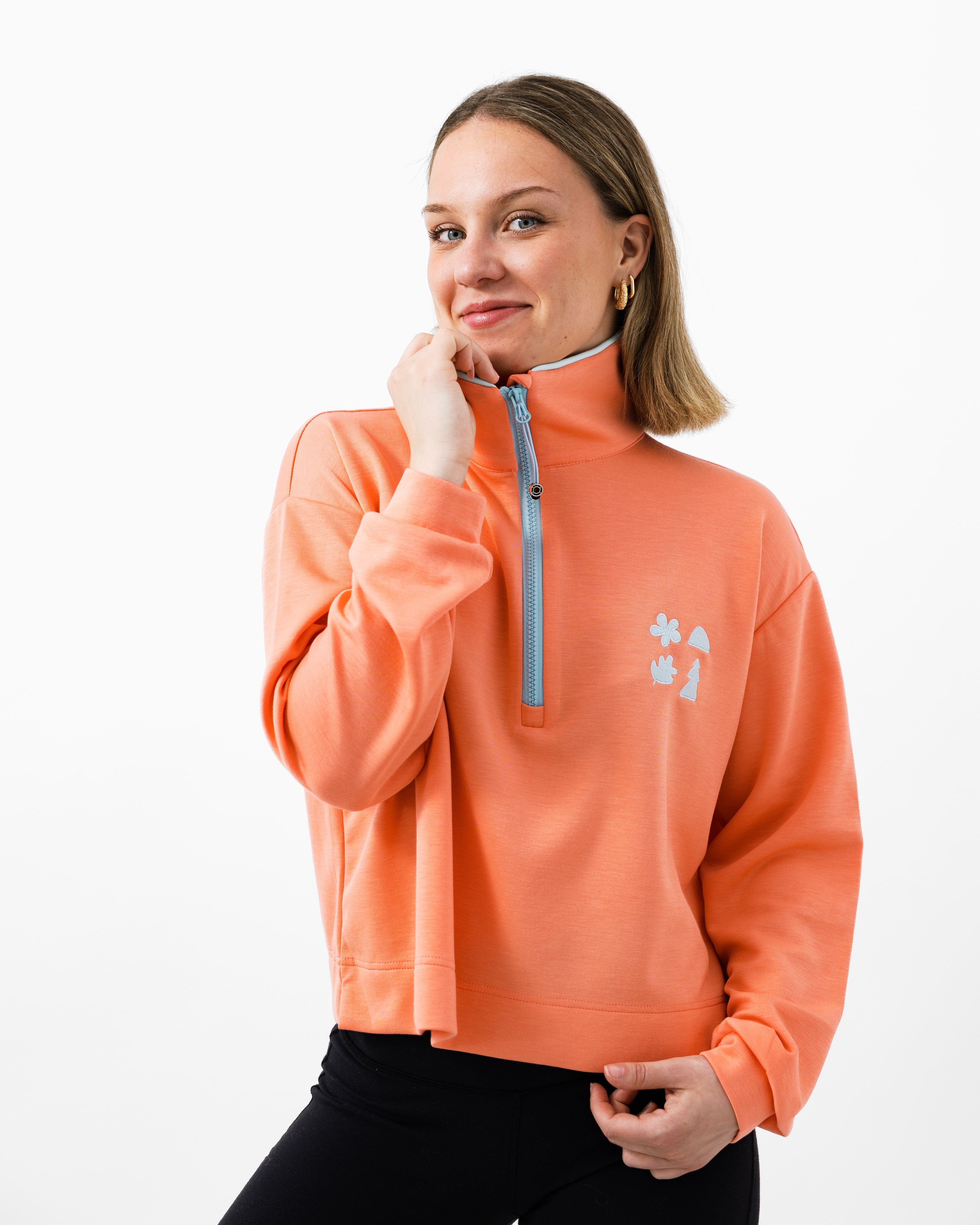 Woman smiling wearing a pink quarter zip with a light blue zipper on a white background