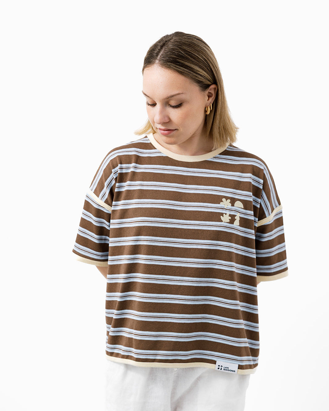 Woman wearing a brown and butter striped t-shirt with small les Saisons icons logo 