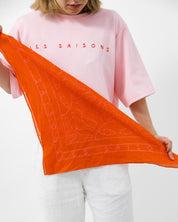 Person holding an orange scarf with 'LES SAISONS' branding against a white background