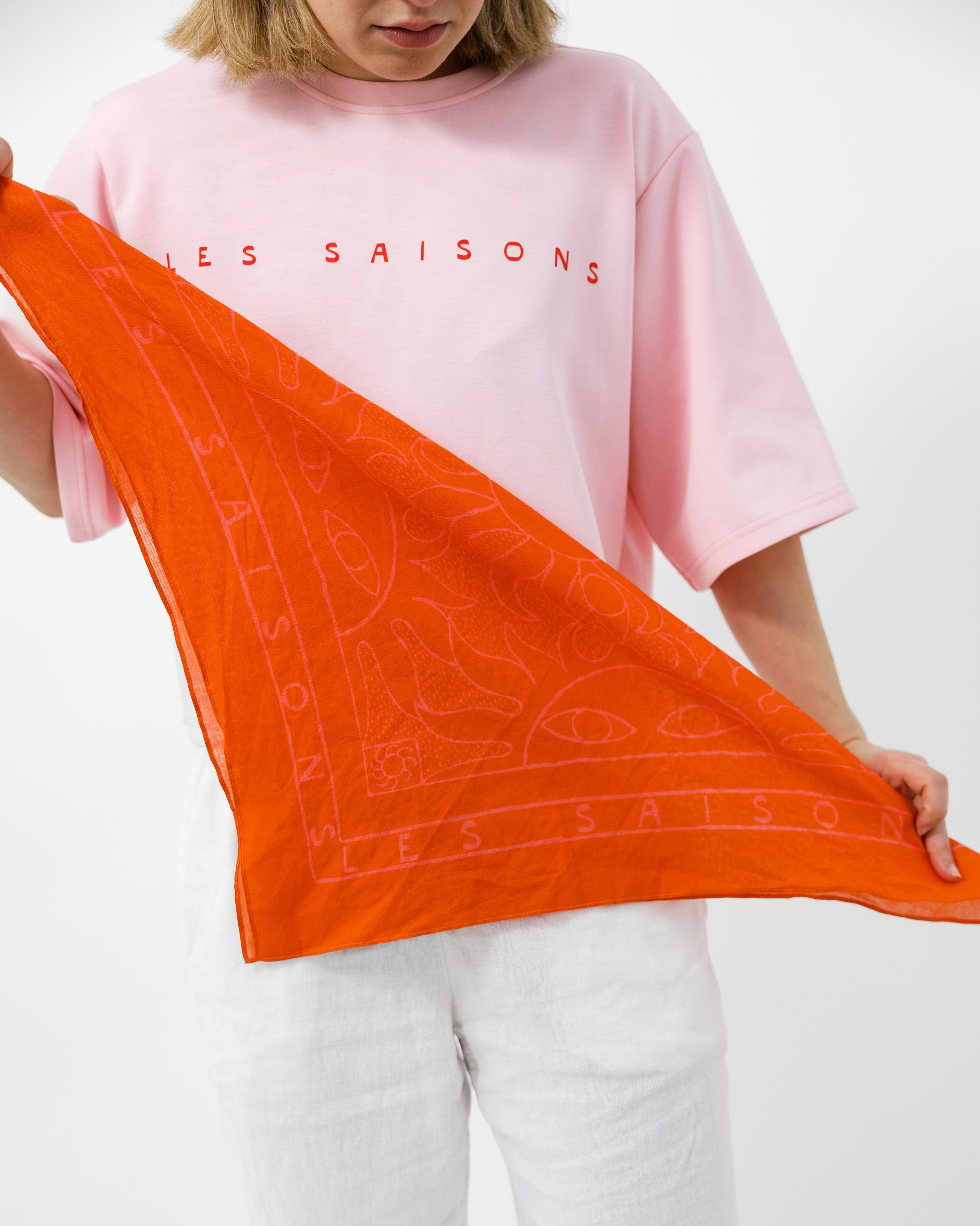 Person holding an orange scarf with 'LES SAISONS' branding against a white background