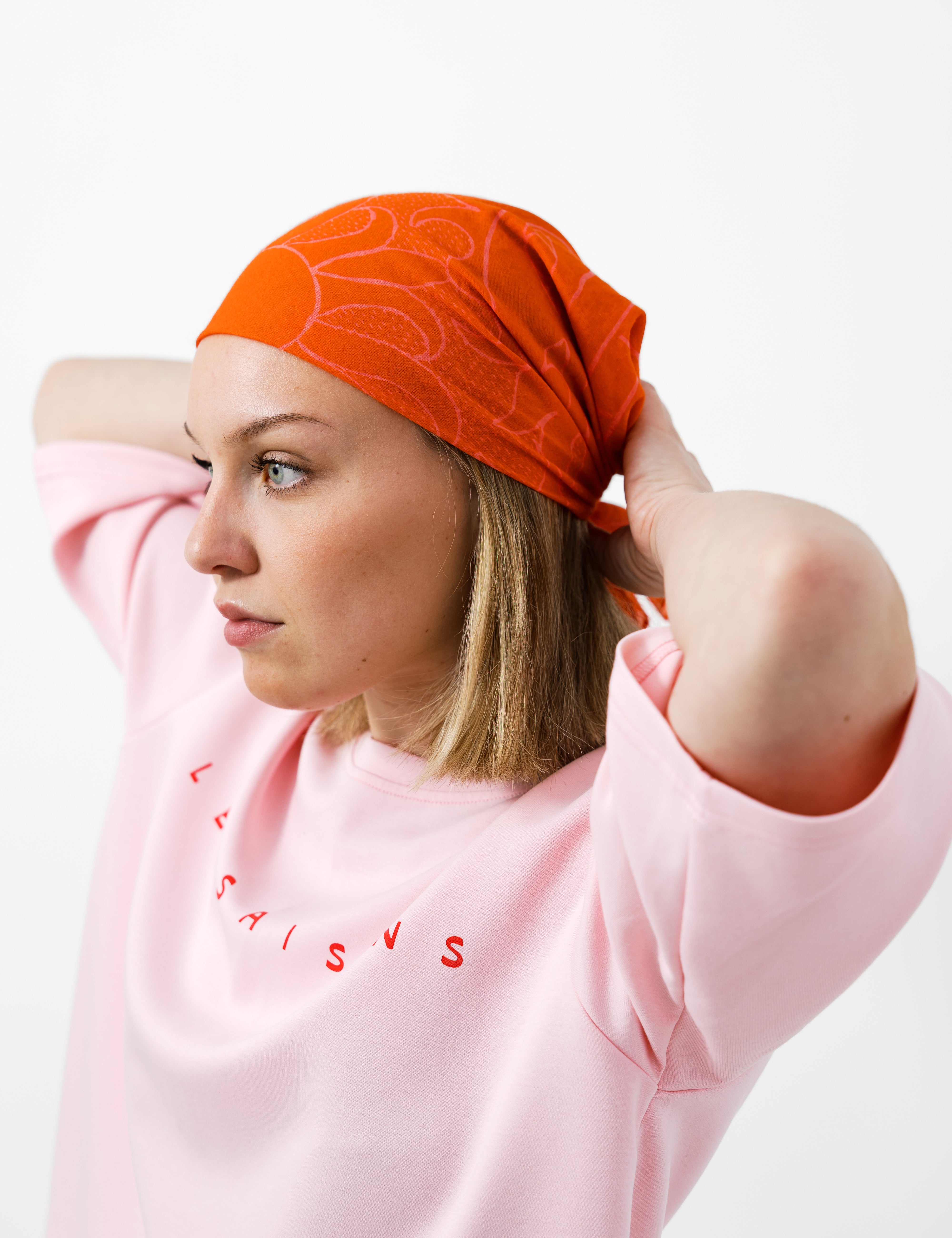 Person wearing a pink t-shirt with les saisons and an orange headscarf on a white background
