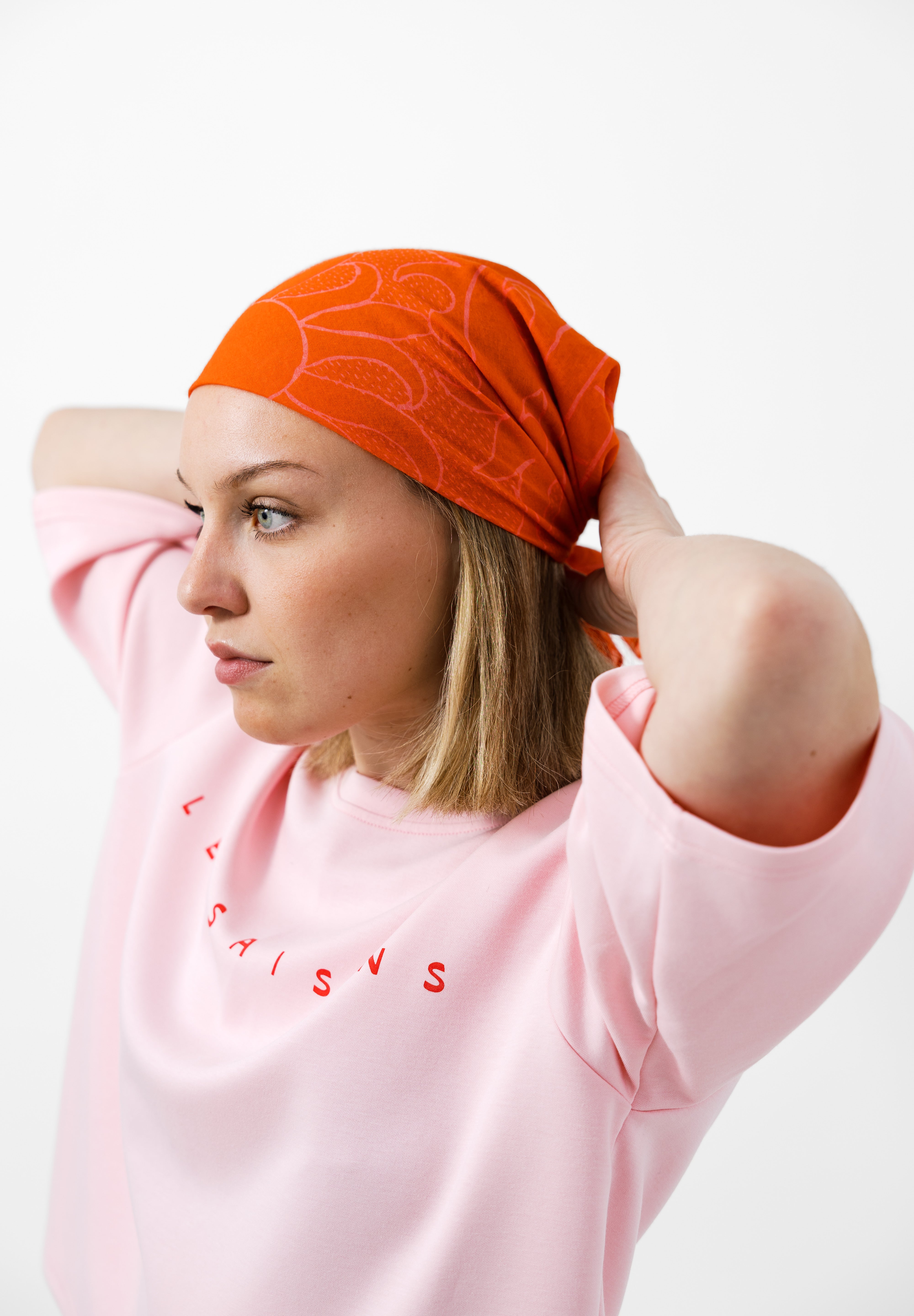 Person wearing a pink t-shirt with les saisons and an orange headscarf on a white background
