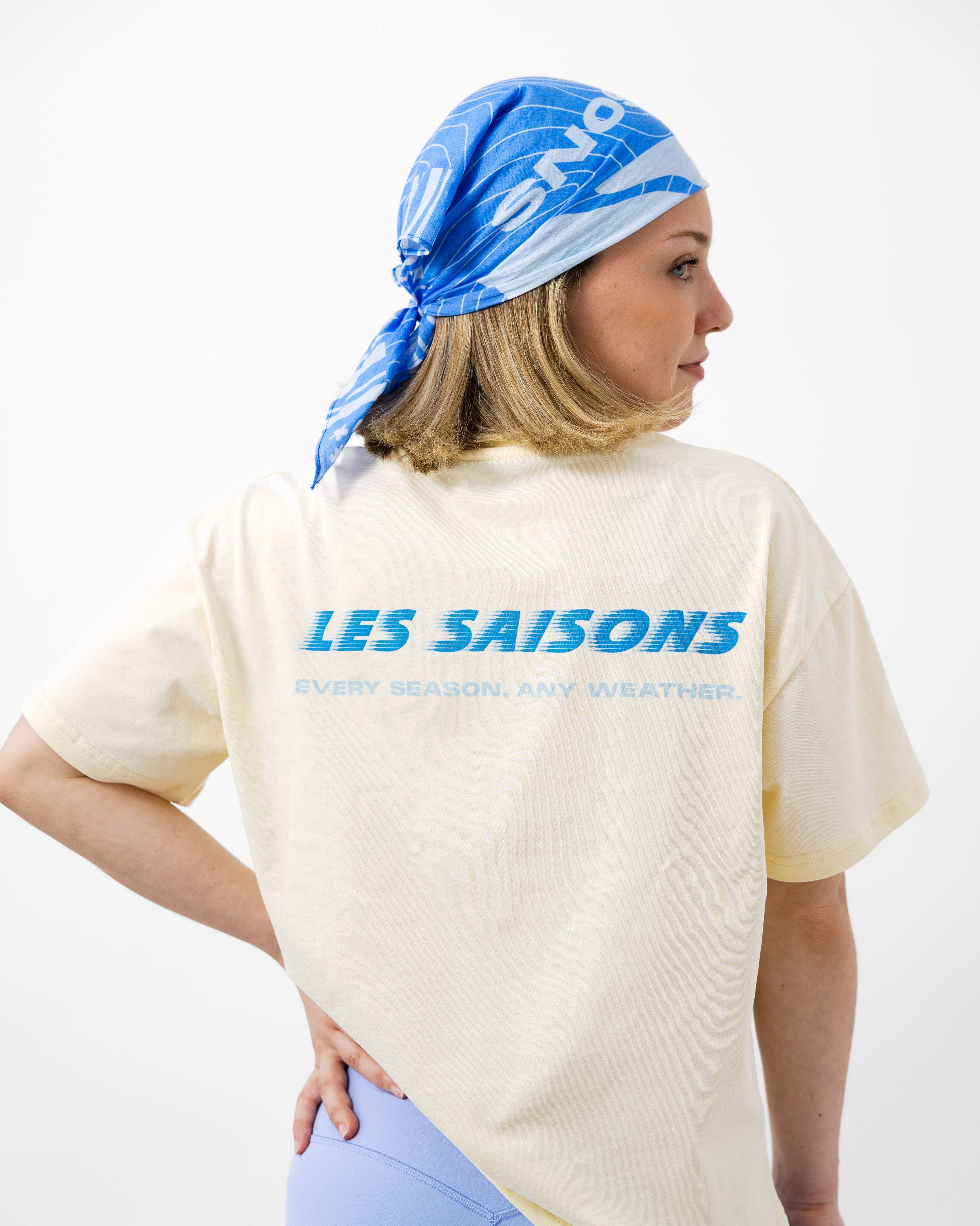 Person wearing a butter t-shirt with 'LES SAISONS' text and a blue headscarf on a white background