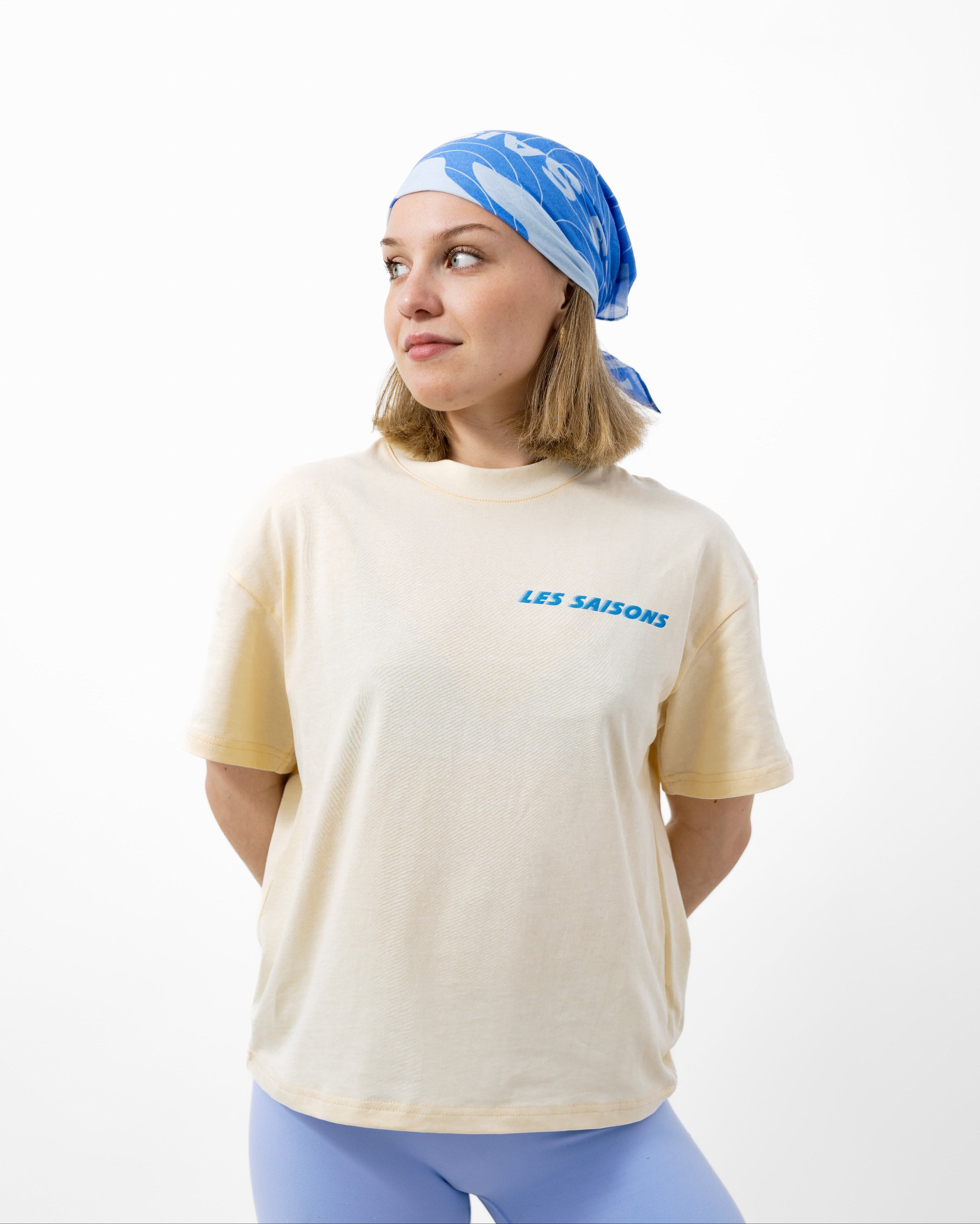Woman wearing a beige t-shirt with blue text and light blue shorts and headscarf on a white background