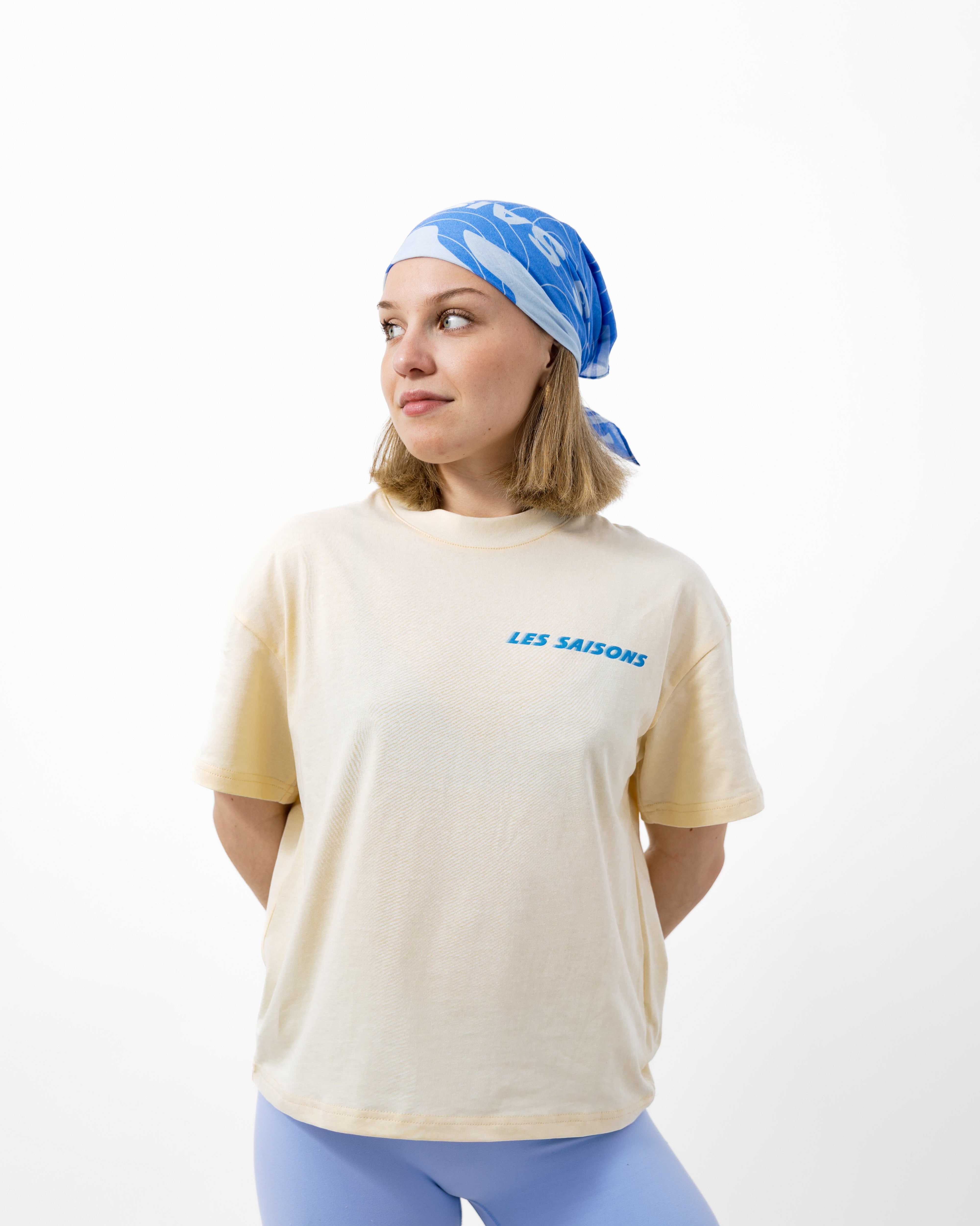 Woman wearing a beige t-shirt with blue text and light blue shorts and headscarf on a white background