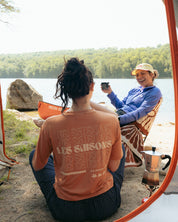 Two women sitting by a lake, one taking a photo, viewed from inside a tent.