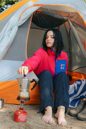 Person camping, sitting inside a tent with a coffee percolator with les Saisons retro Pink fleece jacket