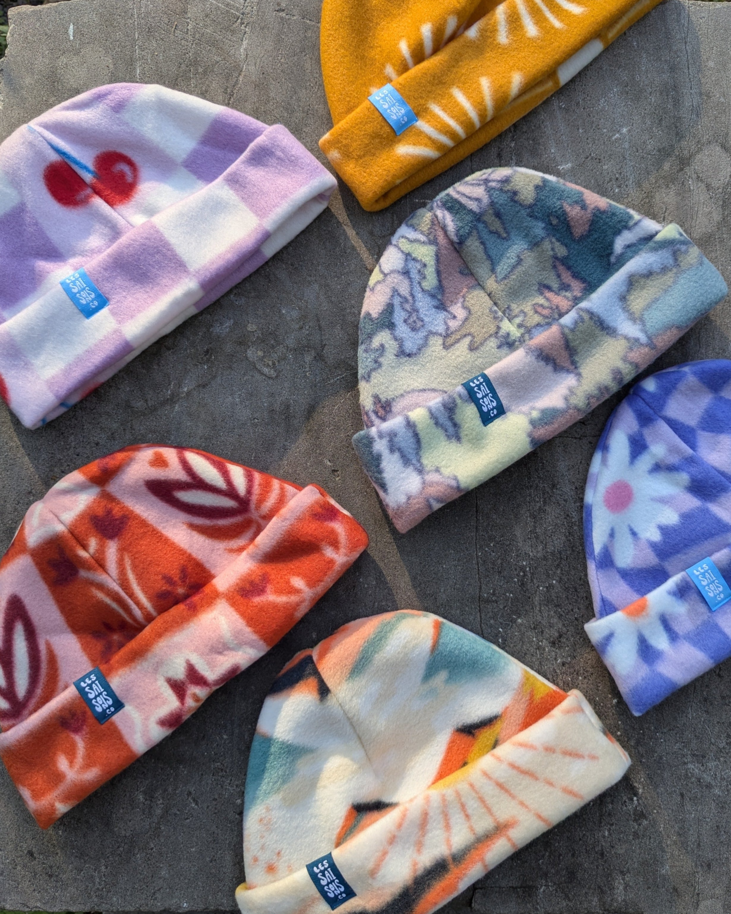 Colorful patterned fleece beanies arranged on a stone surface with a natural background. Perfect for ski and winter