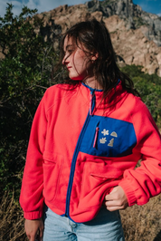 Person wearing a pink jacket with a blue pocket featuring les Saisons logo, outdoors