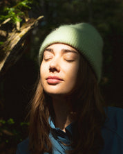Person wearing a green beanie and blue jacket in a forest setting